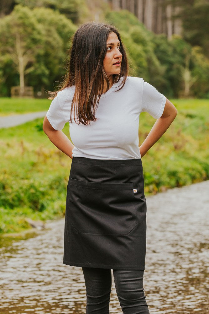 Female model standing outside by a river wearing Bliss Apron Half Length - Black