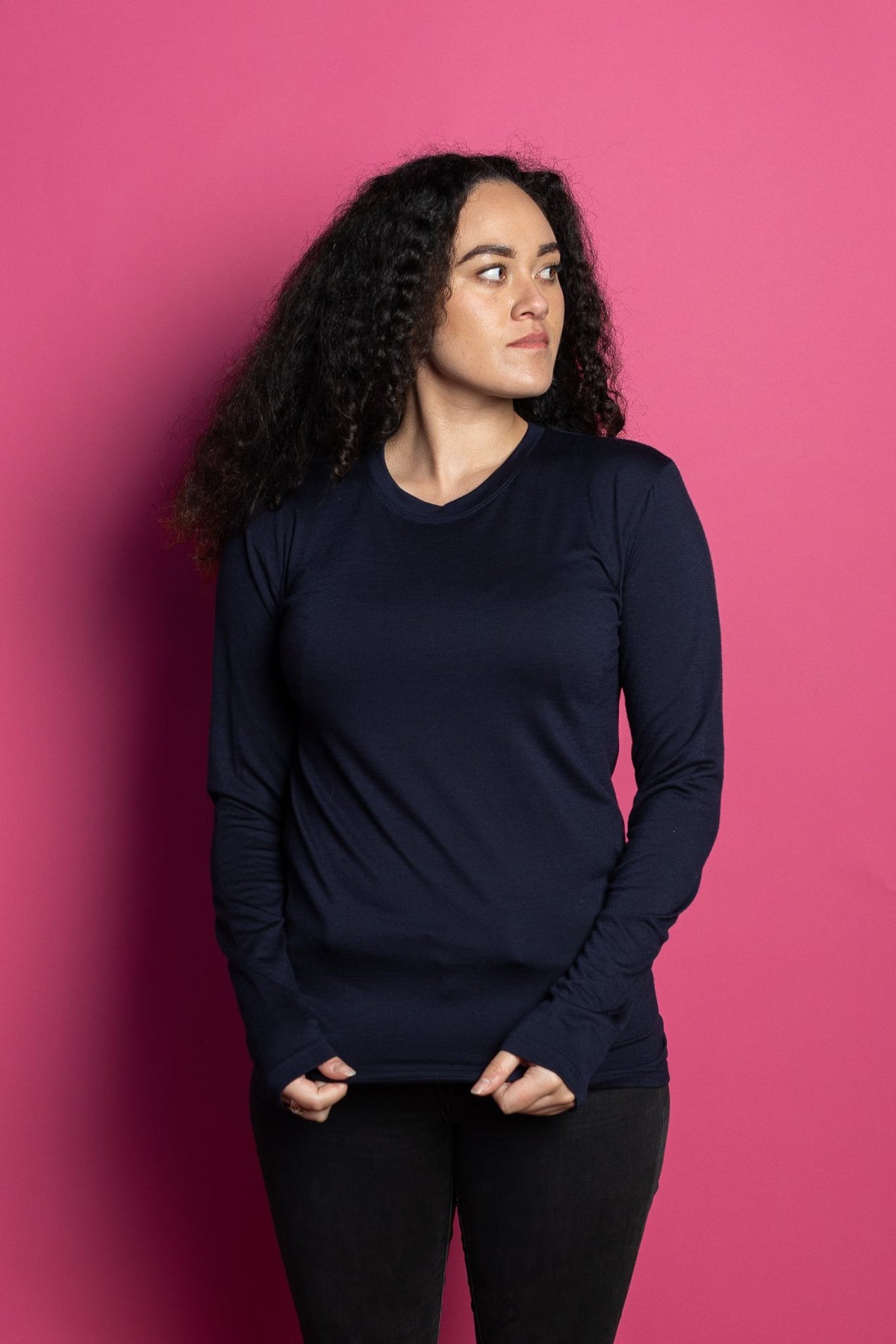 Female model wearing navy marvel merino long sleeve tee against pink background